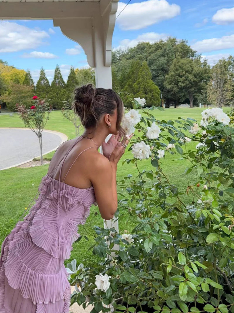 Young woman wearing a lilac ruffled dress standing in a garden, gently smelling white roses – perfect summer outfit inspiration from Isadora London.