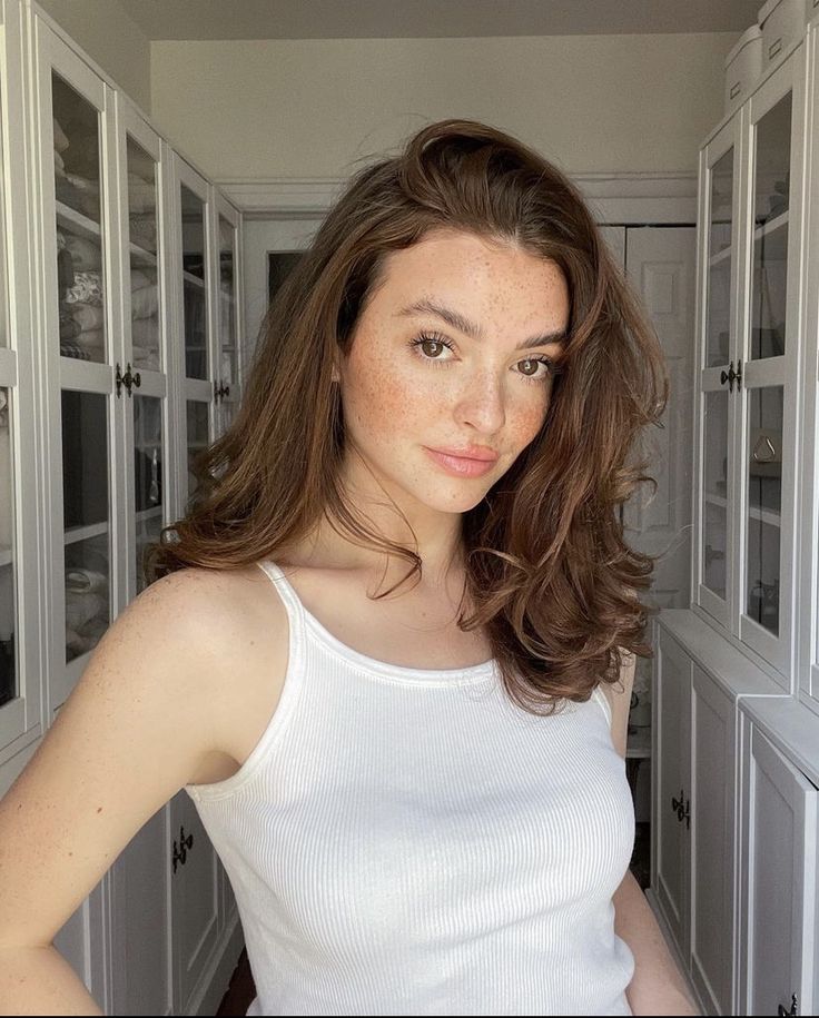 Customer review photo – natural-looking woman with freckles and medium-length brown hair wearing a white tank top, posing confidently indoors in front of white cabinets
