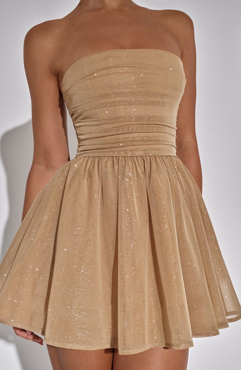 Gold sparkle mini dress with oversized bow at the back – side view with champagne glass