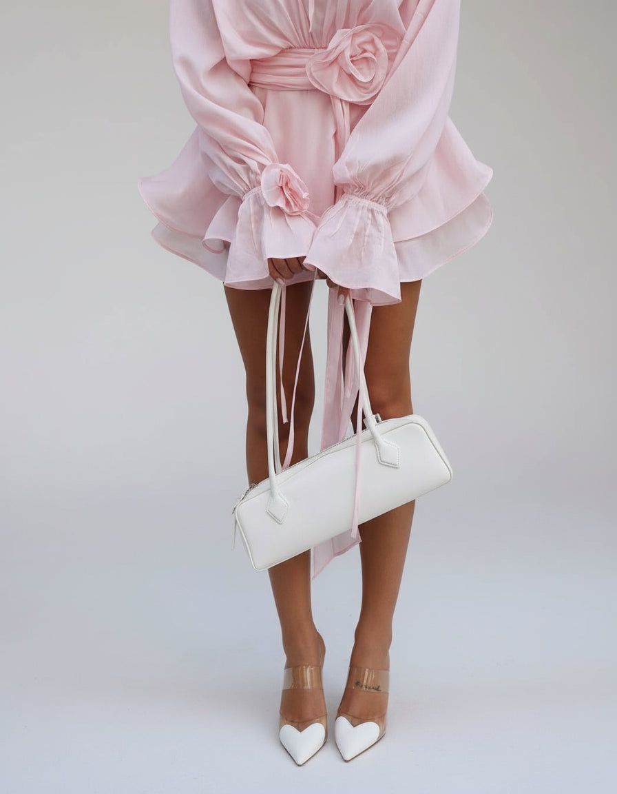 Blonde woman wearing a soft pink flowy mini dress with floral belt detail, walking confidently in sunlight – Isadora London