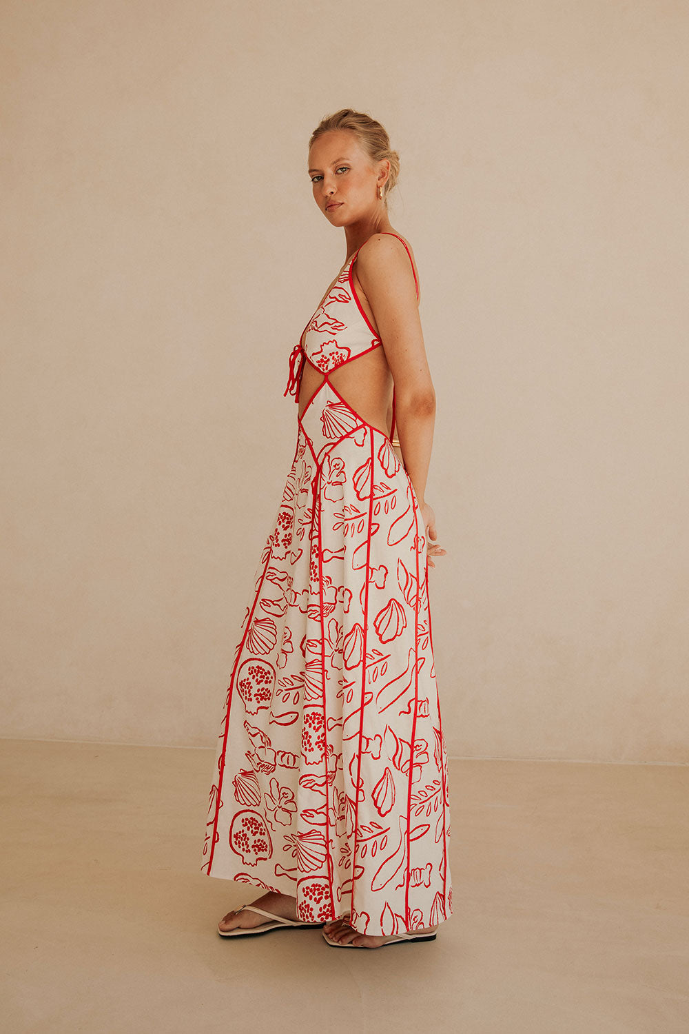 Isadora London Ophelia Maxi Dress – elegant white maxi with red coastal print and waist cut-outs, made for effortless summer style.