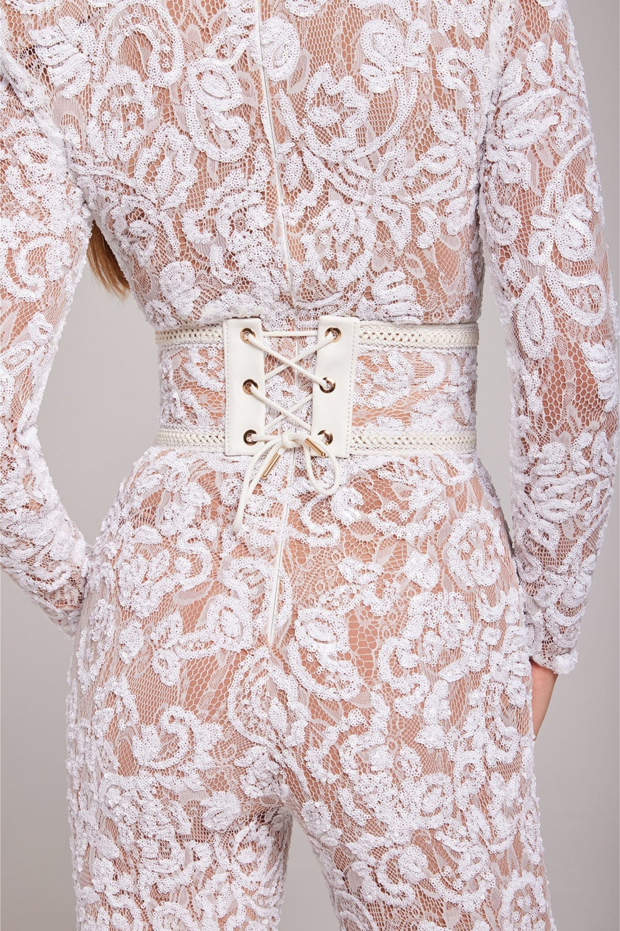 Detail shot of the white lace jumpsuit showing the waistline, floral lace pattern, and structured fit.