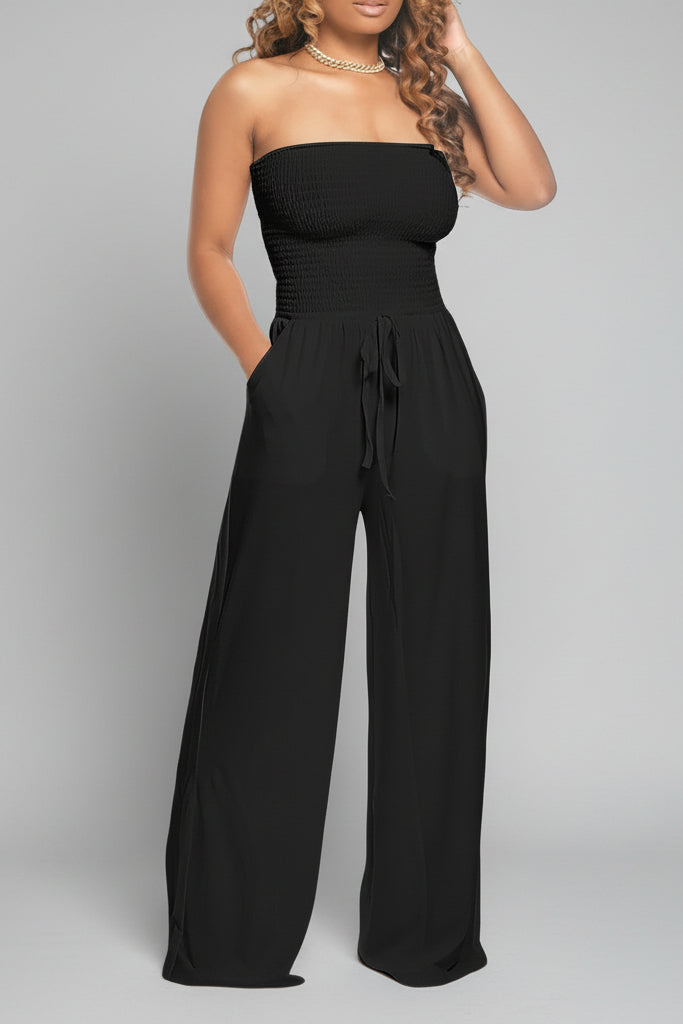 Model wearing a black off shoulder jumpsuit with smocked bodice, wide-leg fit and tie-waist – casual and flattering style.