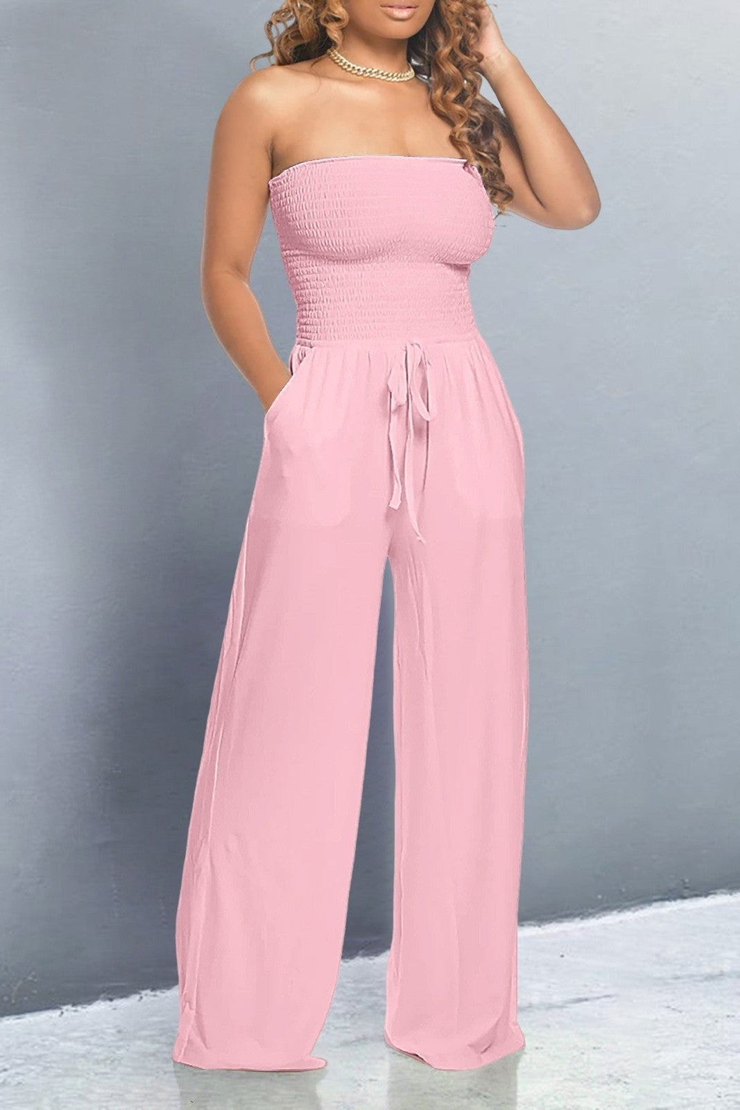Model wearing a pink off shoulder jumpsuit with smocked bodice, wide-leg fit and tie-waist – casual and flattering style.