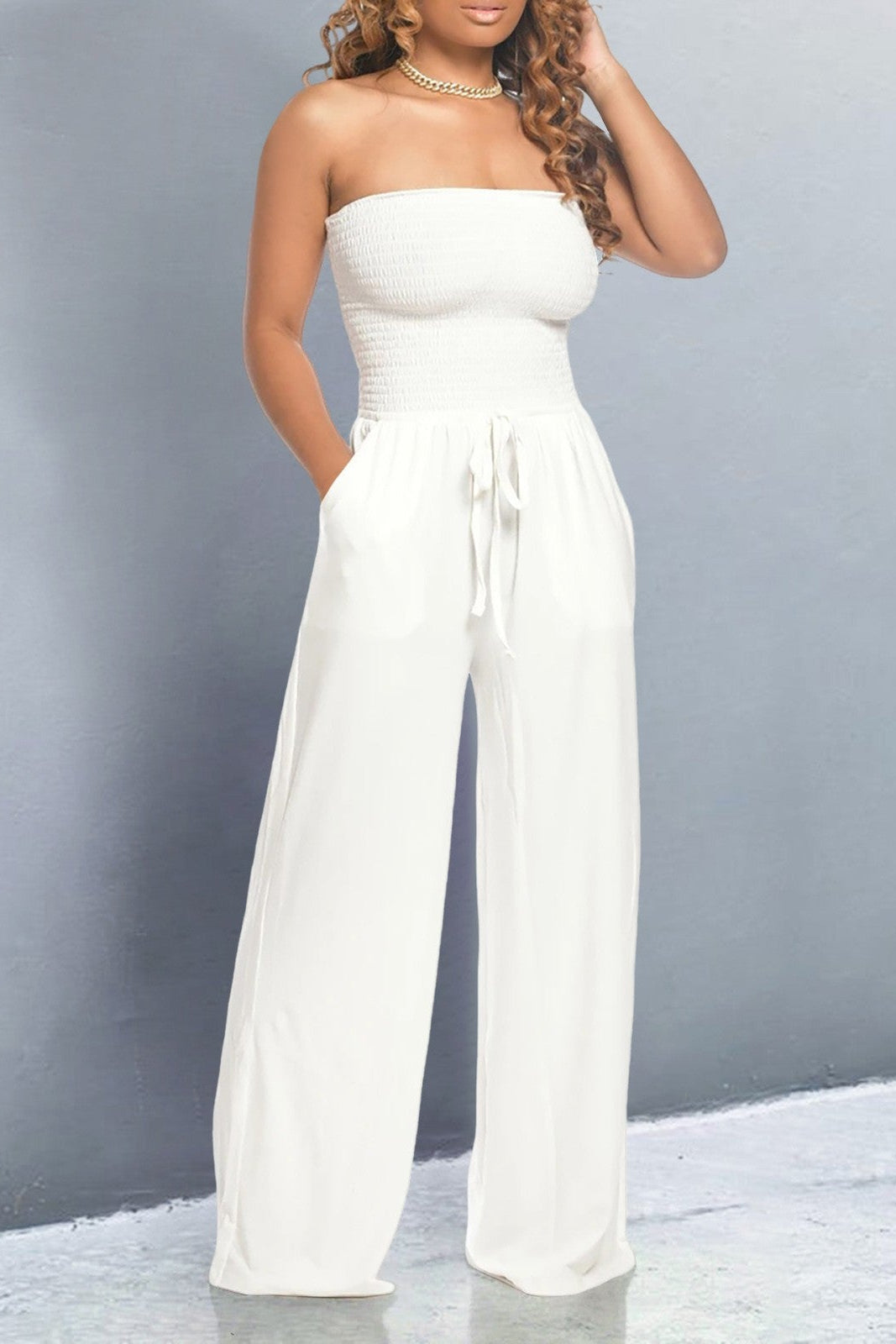 Model wearing a white off shoulder jumpsuit with smocked bodice, wide-leg fit and tie-waist – casual and flattering style.